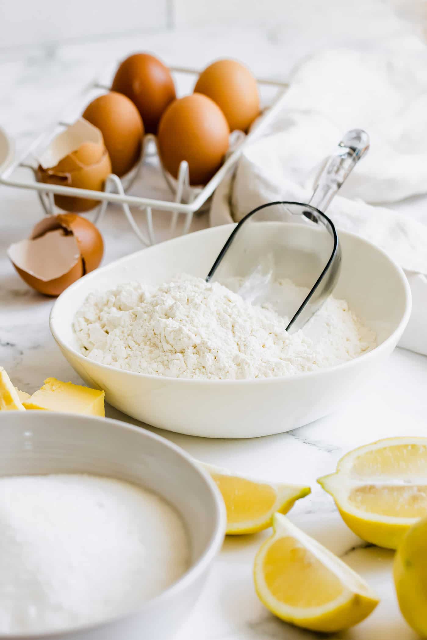 bowls of flour and sugar, plus fresh lemons, cubes of butter, and eggs