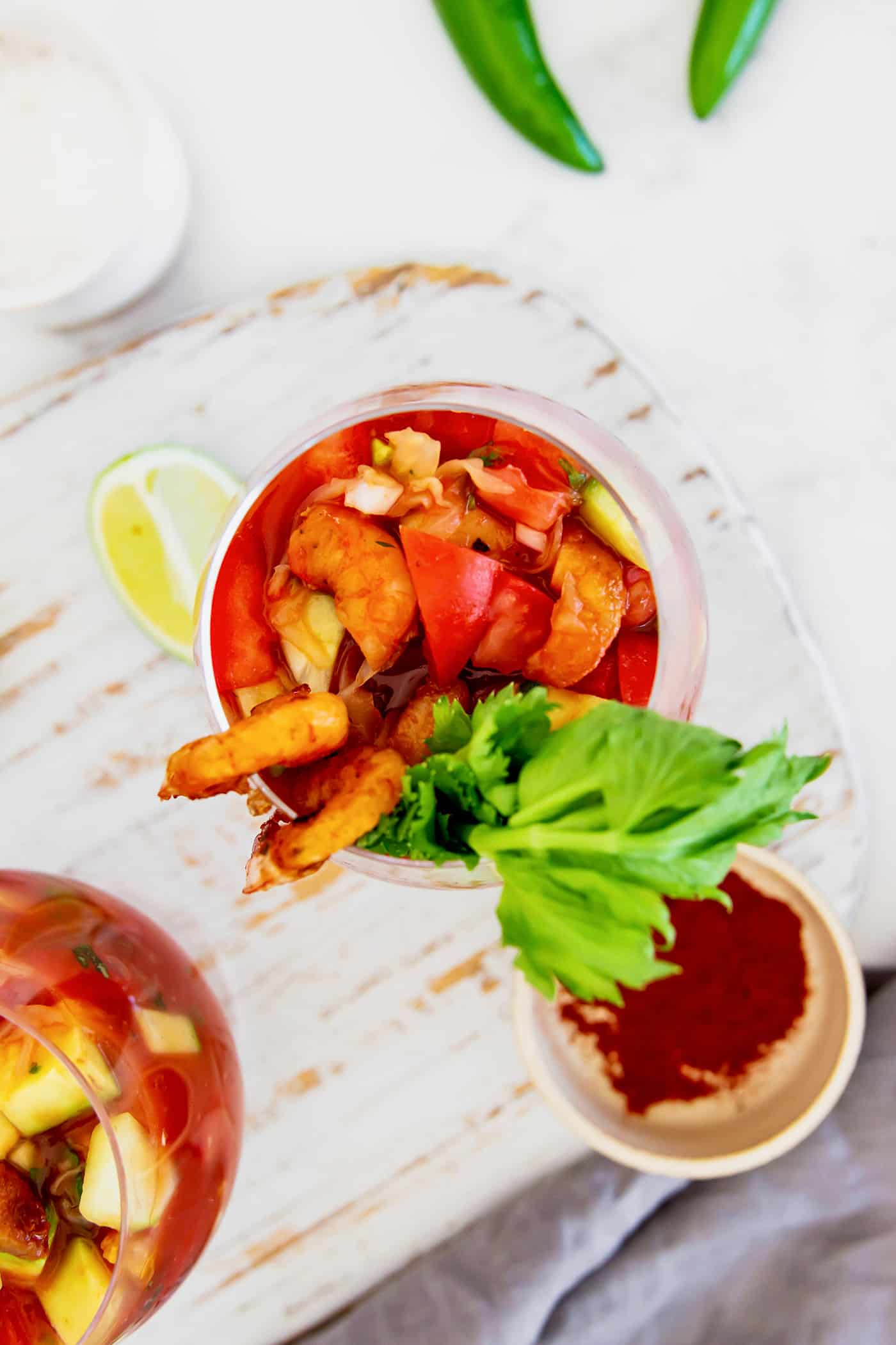 overhead photo of two glasses of appetizers with tomato juice, lime, and shrimp