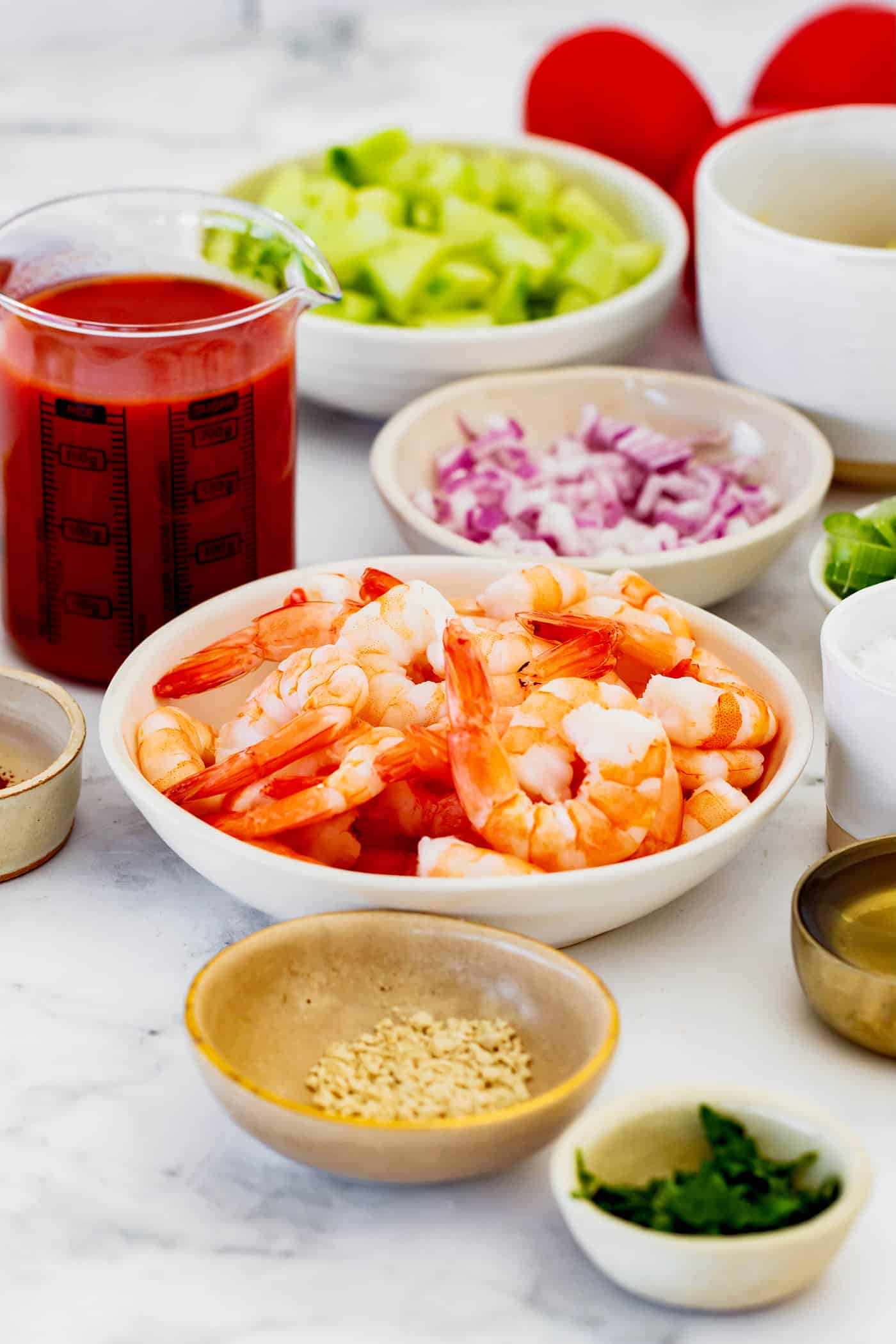 ingredients for shrimp cocktail, including shrimp, diced avocado and red onion, and tomato juice