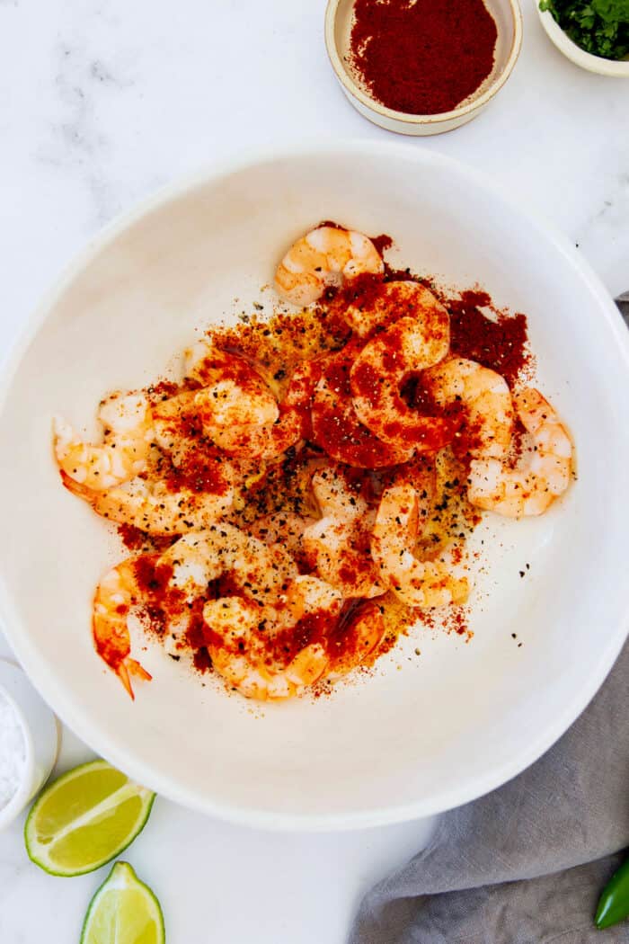 shrimp in a white bowl, sprinkled with chili powder, garlic powder, and smoked paprika