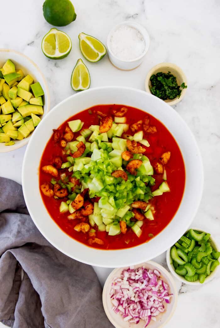 combining a red cocktail sauce with cooked shrimp and diced vegetables in a large white bowl