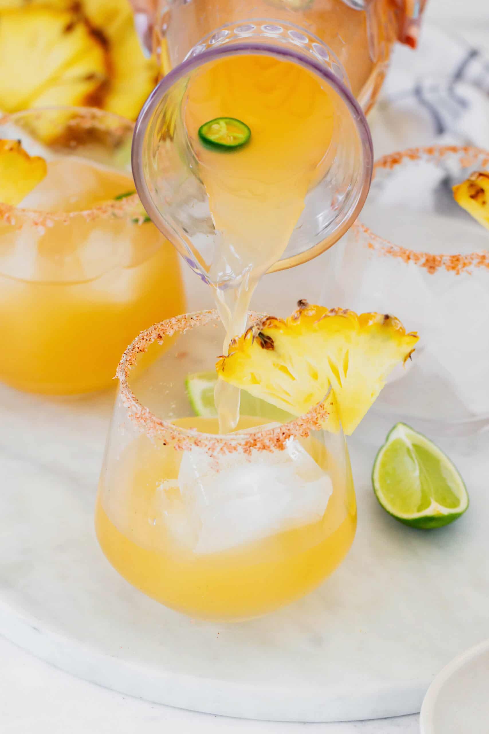 pouring pineapple jalapeno margarita mixture from a pitcher to a glass