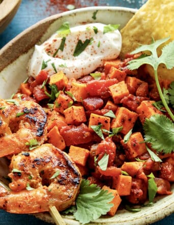 a pottery bowl with a skewer of grilled shrimp and diced sweet potatoes and tomatoes