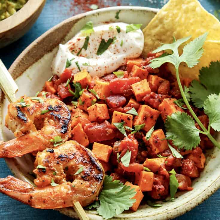 a pottery bowl with a skewer of grilled shrimp and diced sweet potatoes and tomatoes