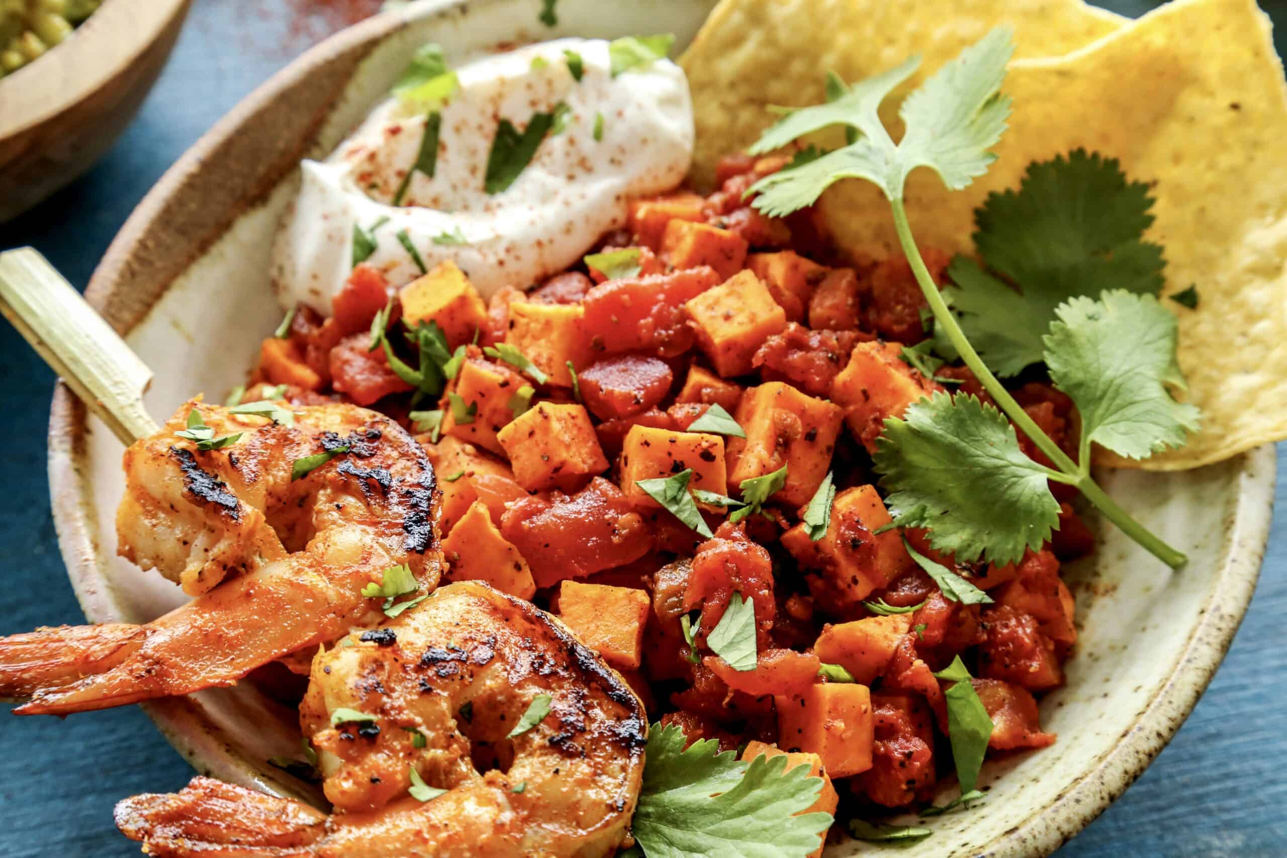 a pottery bowl of diced sweet potatoes and tomatoes, plus a small skewer of grilled shrimp