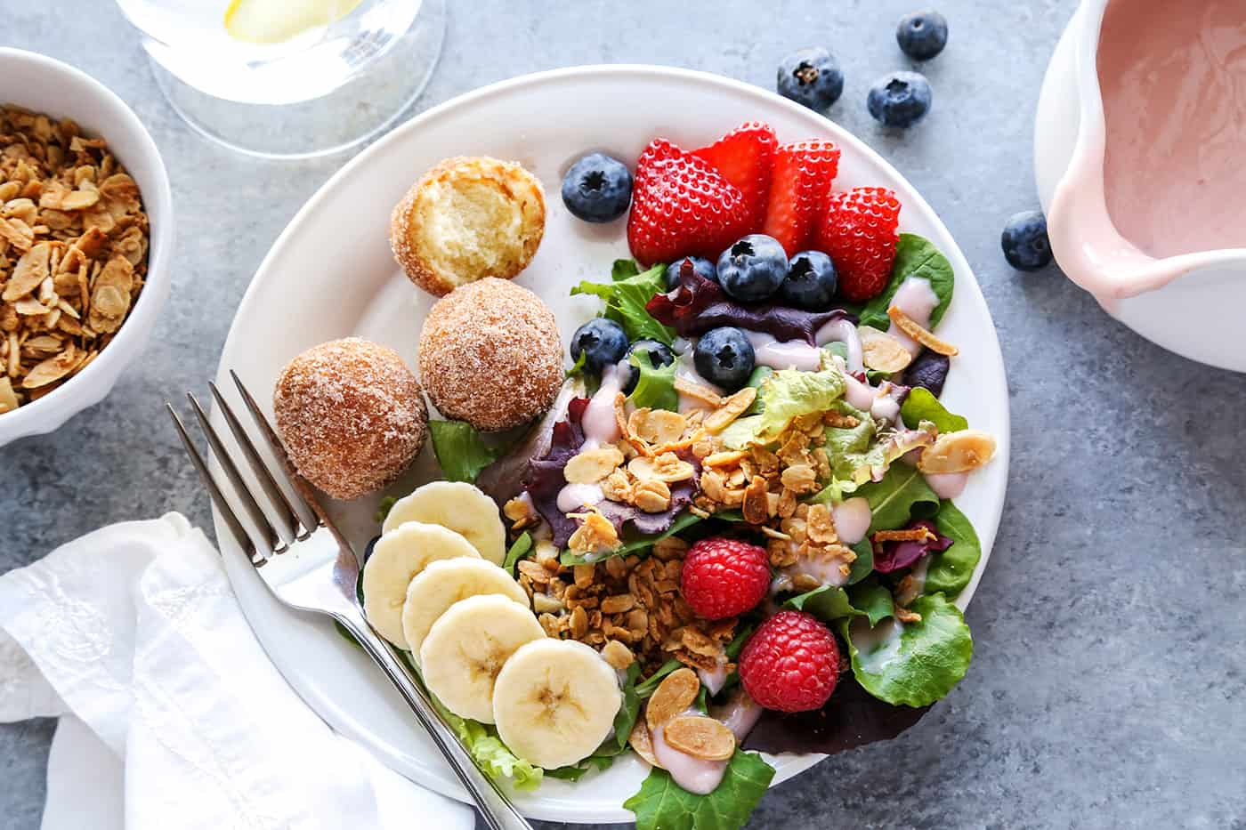 Overhead view of a plate of Breakfast Salad topped with granola and served with a few donut holes