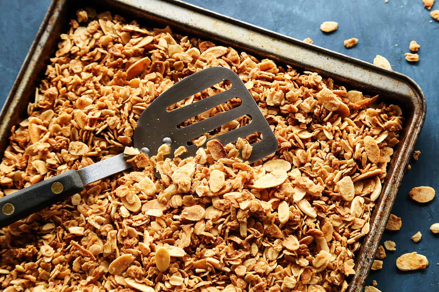 A sheet pan of homemade granola with a spatula