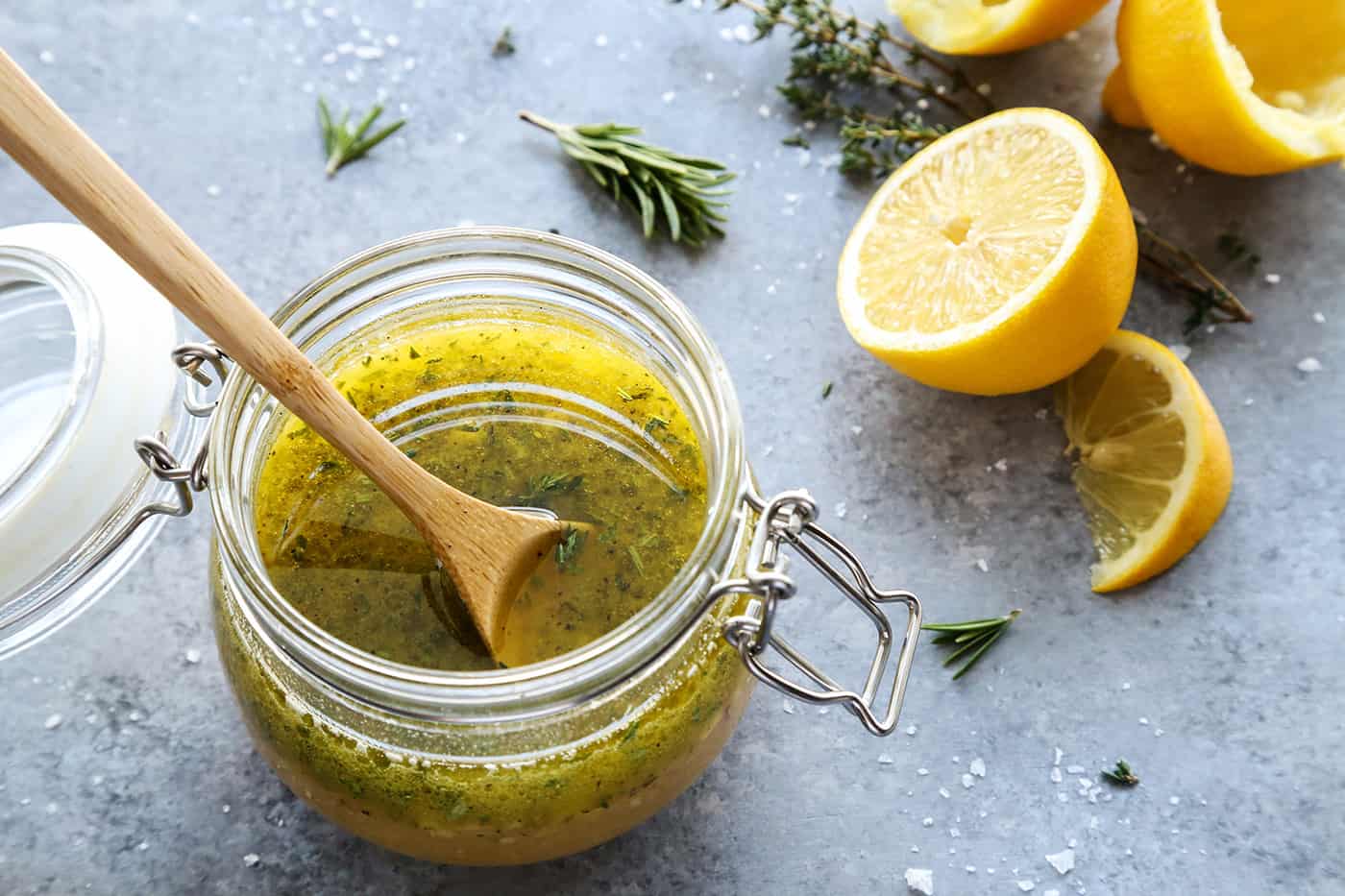 A small jar of homemade lemon herb vinaigrette with a wooden spoon