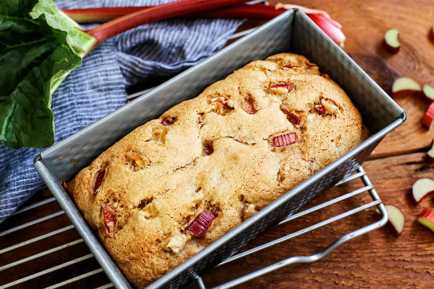 A loaf of Cinnamon Rhubarb Bread in a pan on a cooling rack