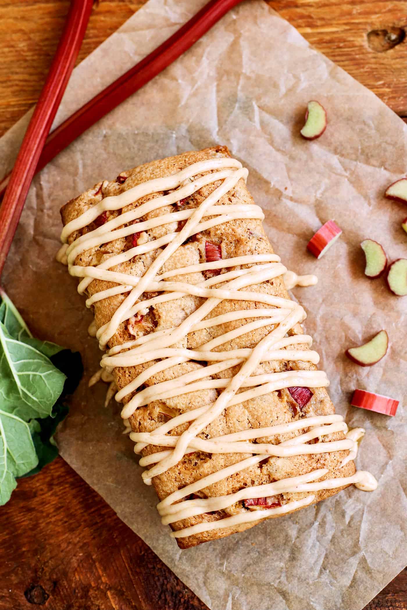 Overhead view of a loaf of Cinnamon Rhubarb Bread drizzled with glaze on parchment paper