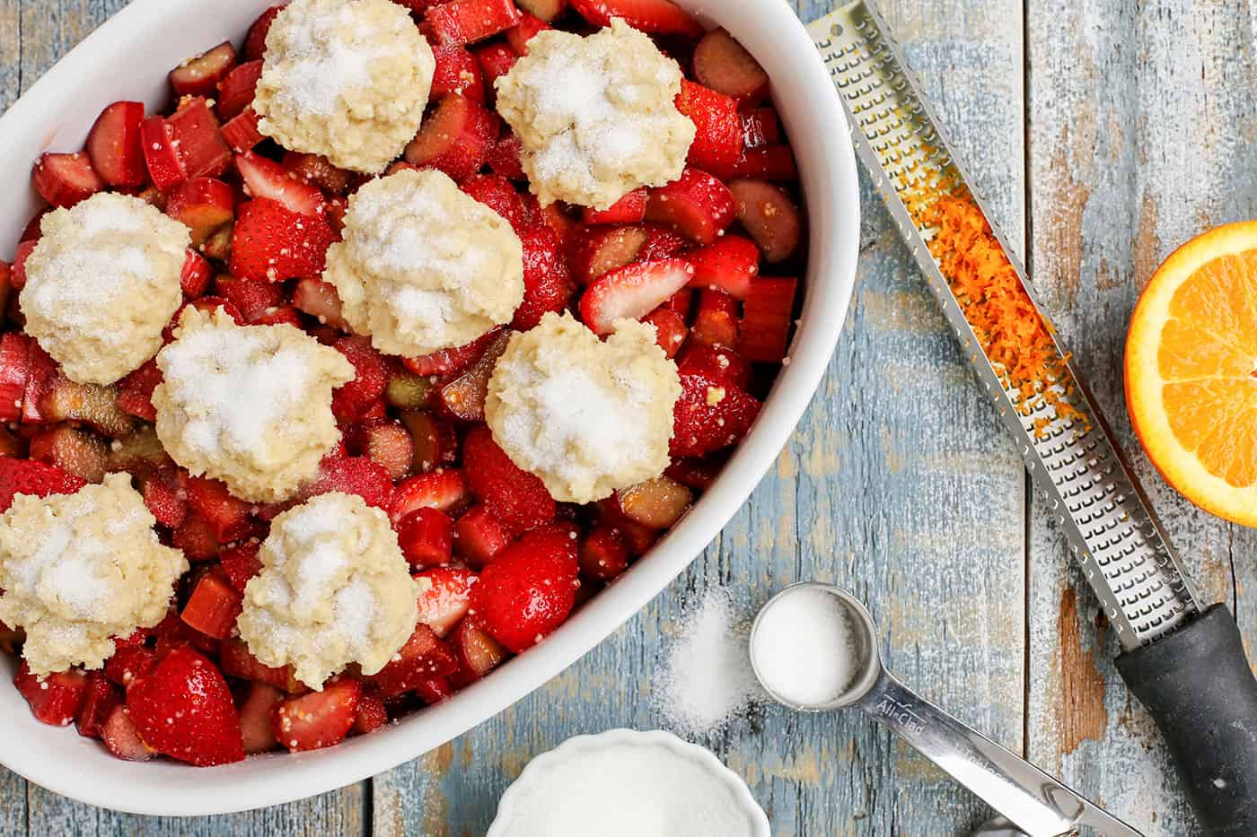 Unbaked Strawberry Rhubarb Cobbler in an oval baking dish next to ingredients