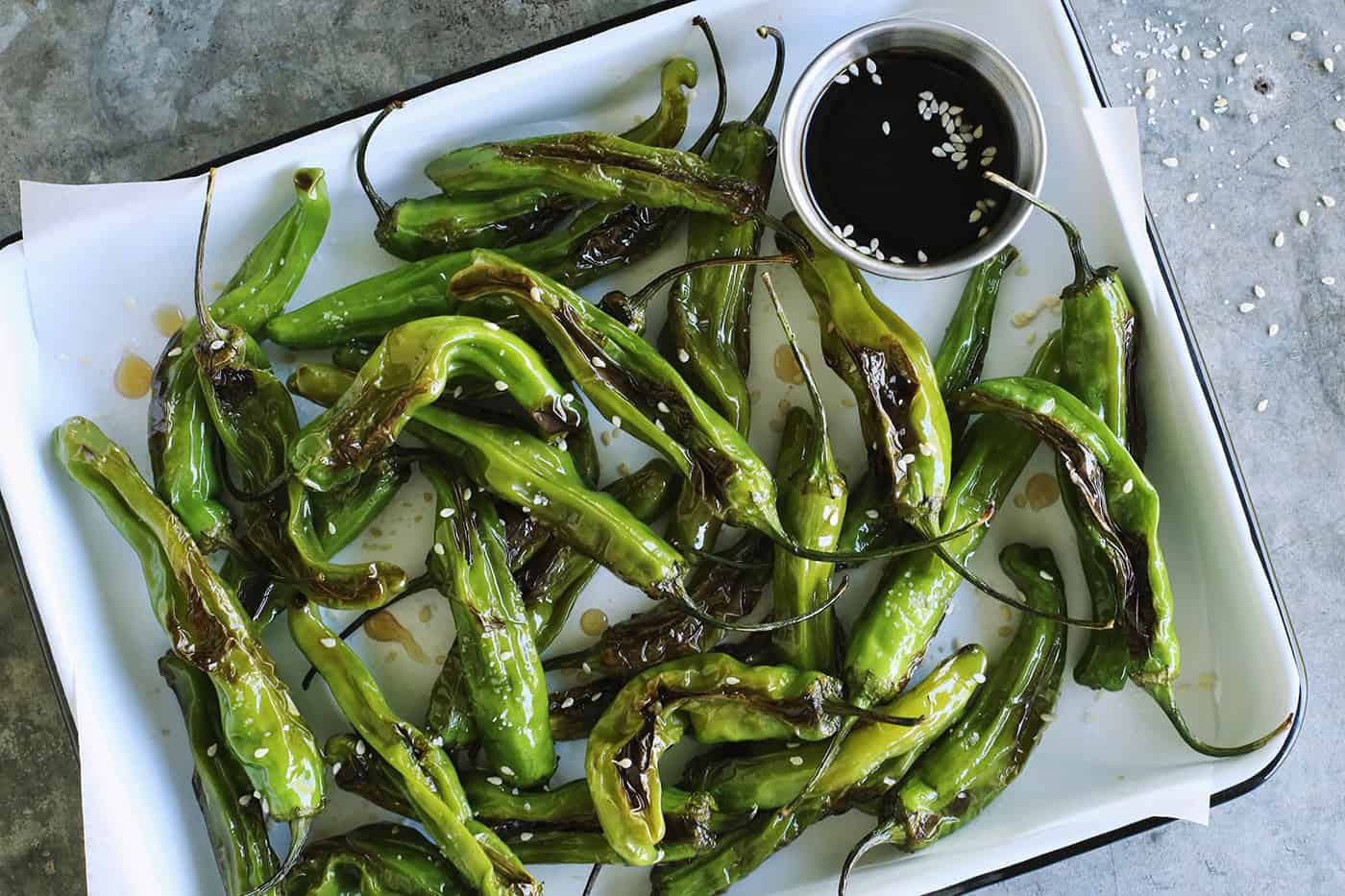 blistered shishitos on a rectangular white enamel pan with soy honey sauce