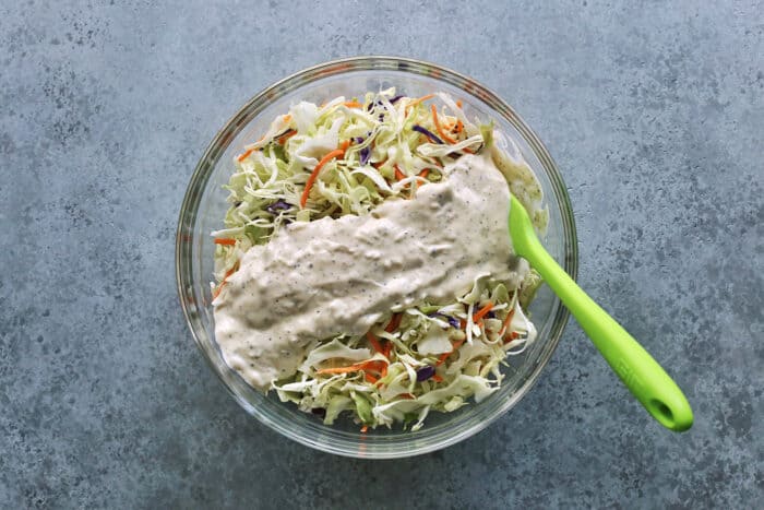 creamy dressing poured over shredded coleslaw mix in a clear bowl