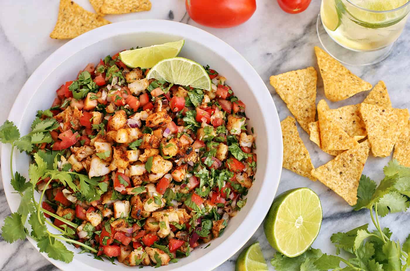 Overhead view of a large white bowl of Grilled Shrimp Ceviche next to tortilla chips, lime and cilantro