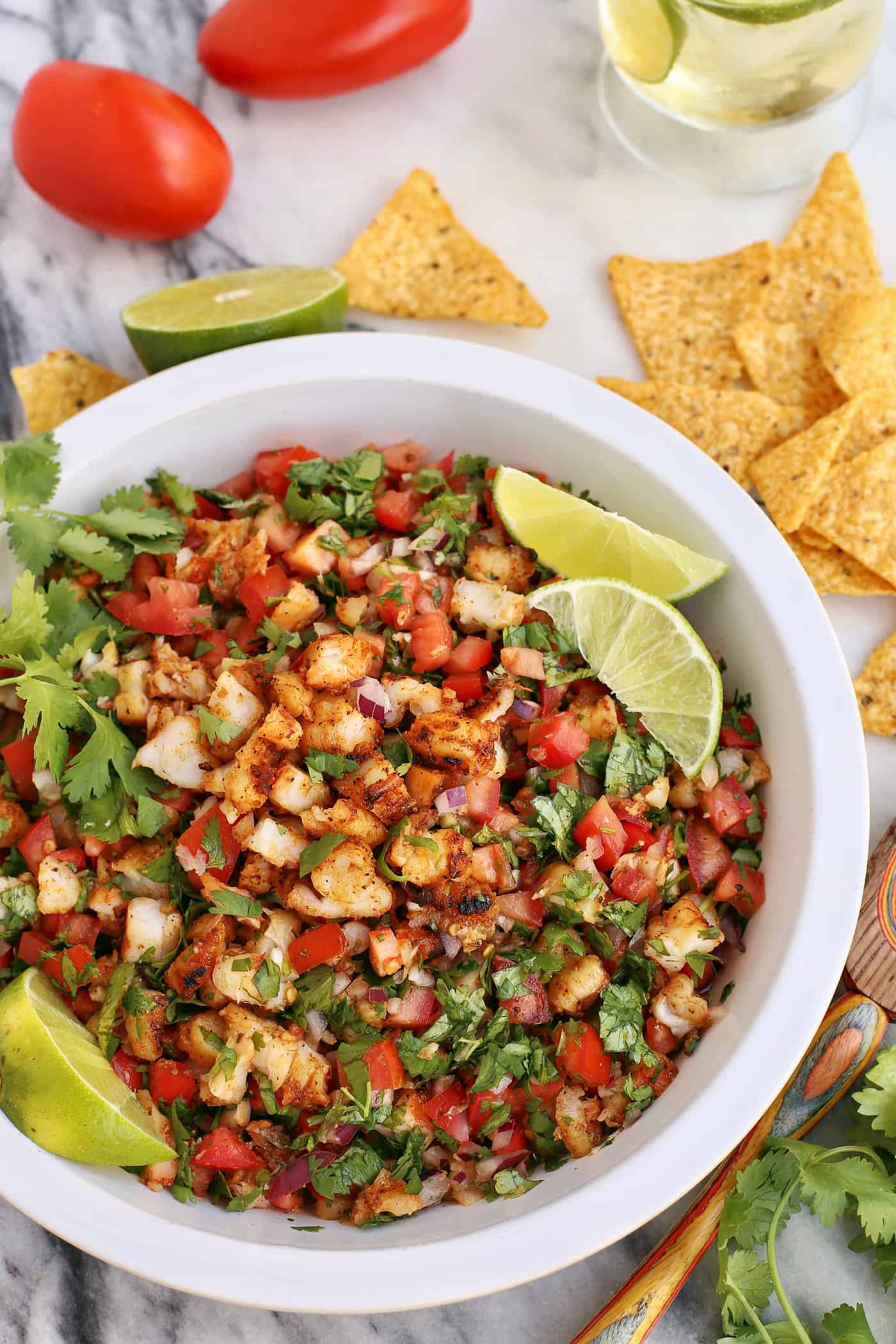 Grilled Shrimp Ceviche in a large white bowl with lime wedges and surrounded by tortilla chips and ingredients