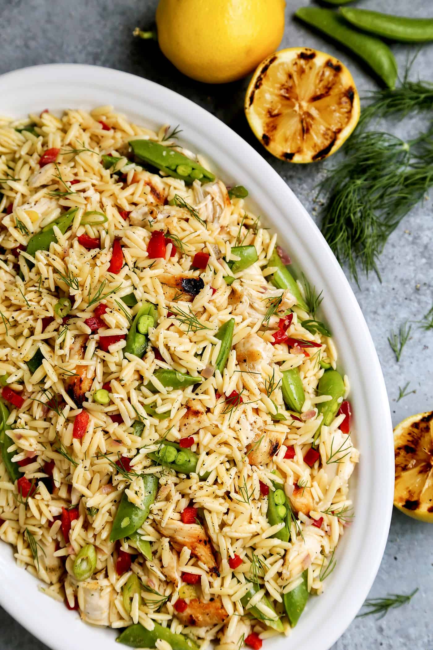 Overhead view of Grilled Chicken and Lemon Orzo salad in a big white bowl with ingredients around it