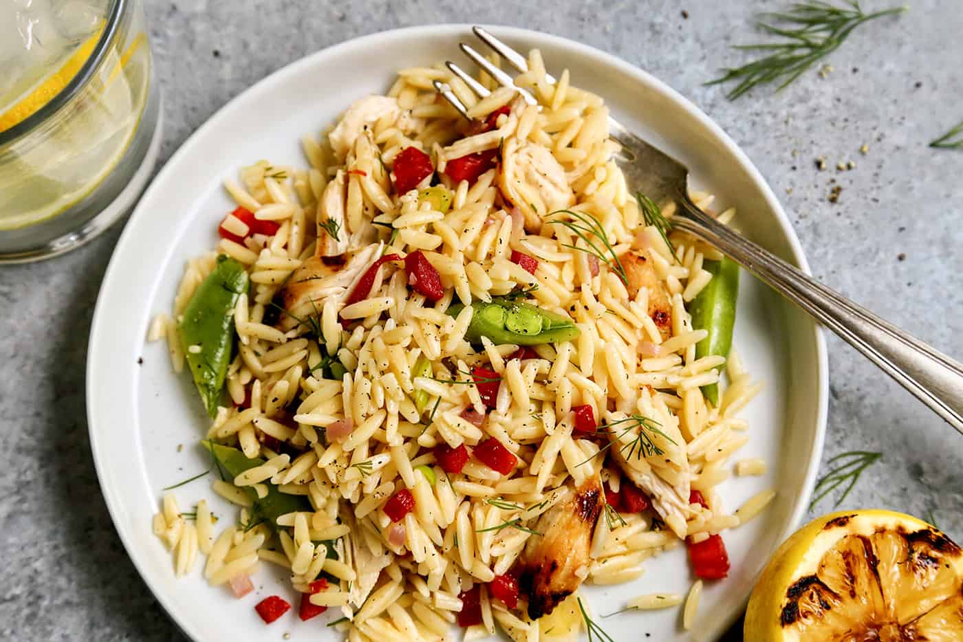 Overhead view of a serving of Grilled Chicken Lemon Orzo salad on a white plate with a fork