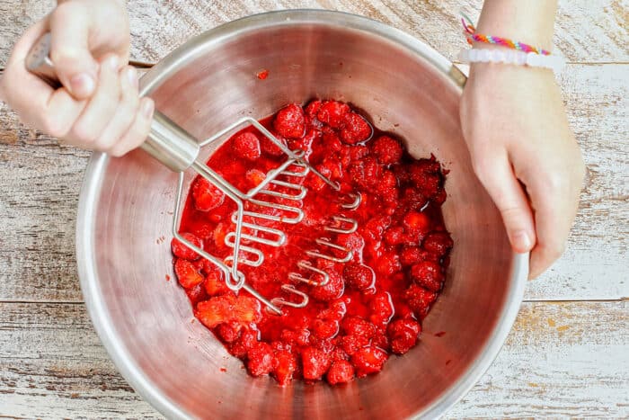 Strawberries being mashed in a bowl.