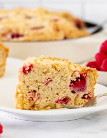 a piece of coffee cake with raspberries and rhubarb, on a white plate with a fork