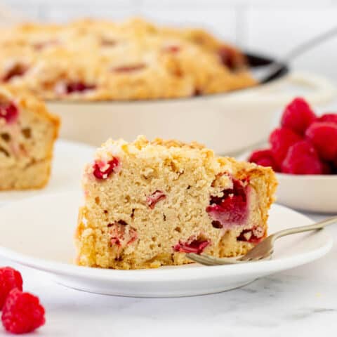 a piece of coffee cake with raspberries and rhubarb, on a white plate with a fork