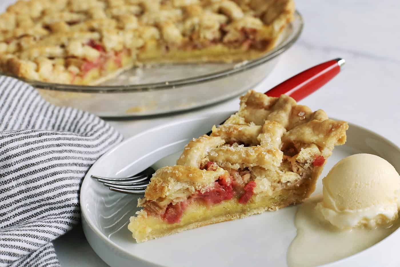 rhubarb pie with custard layer on a white plate, with a scoop of ice cream