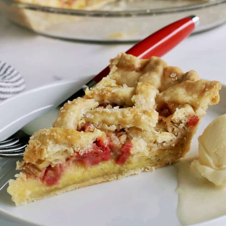 a slice of rhubarb custard pie on a white plate with a scoop of ice cream
