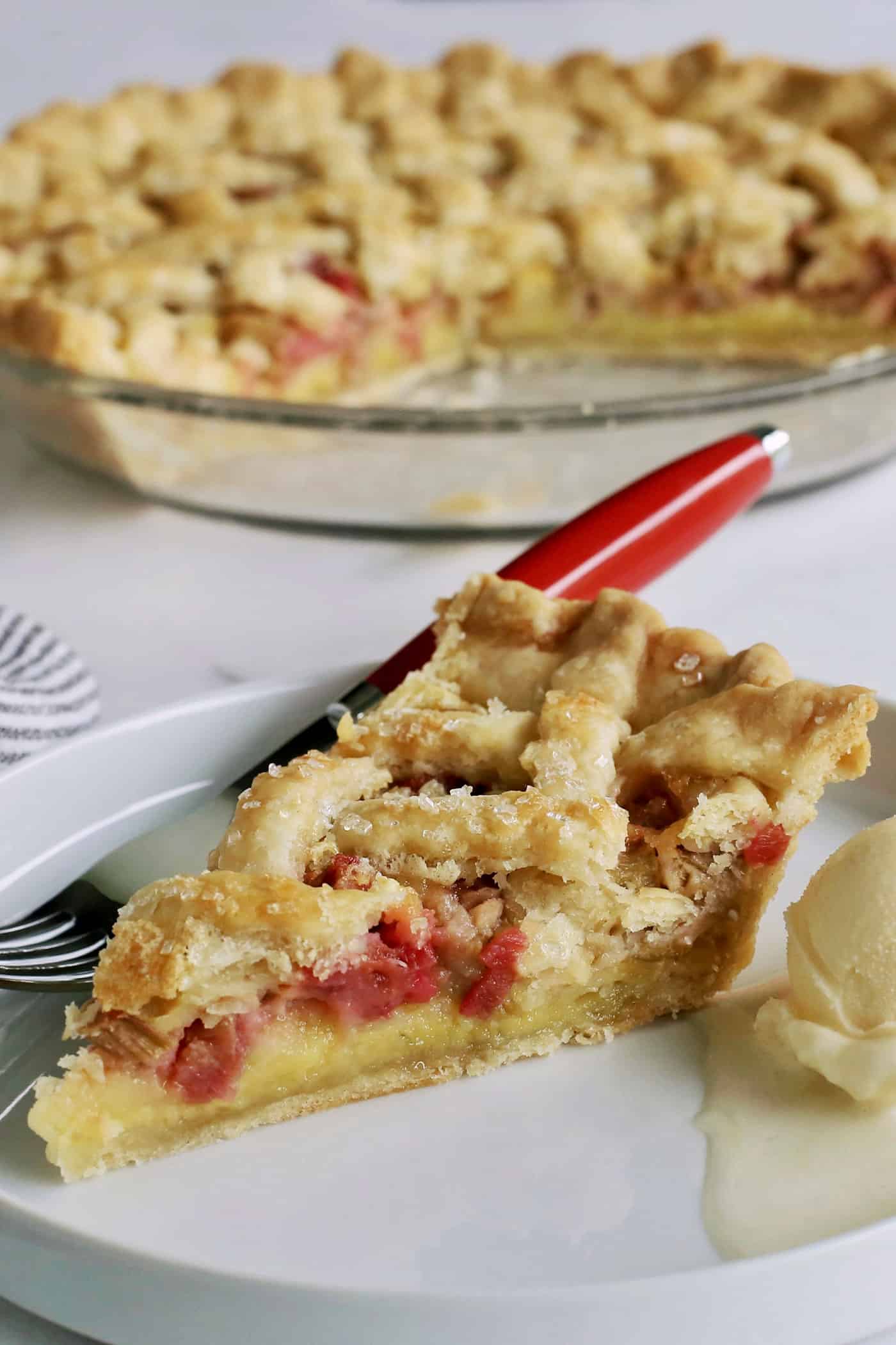 a slice of rhubarb custard pie on a white plate, with the pie plate in the background