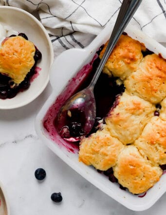 a square white pan of blueberry cobbler with individual servings in smaller bowls
