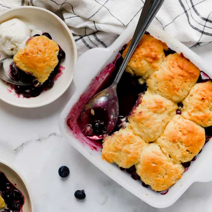 a square white pan of blueberry cobbler with individual servings in smaller bowls