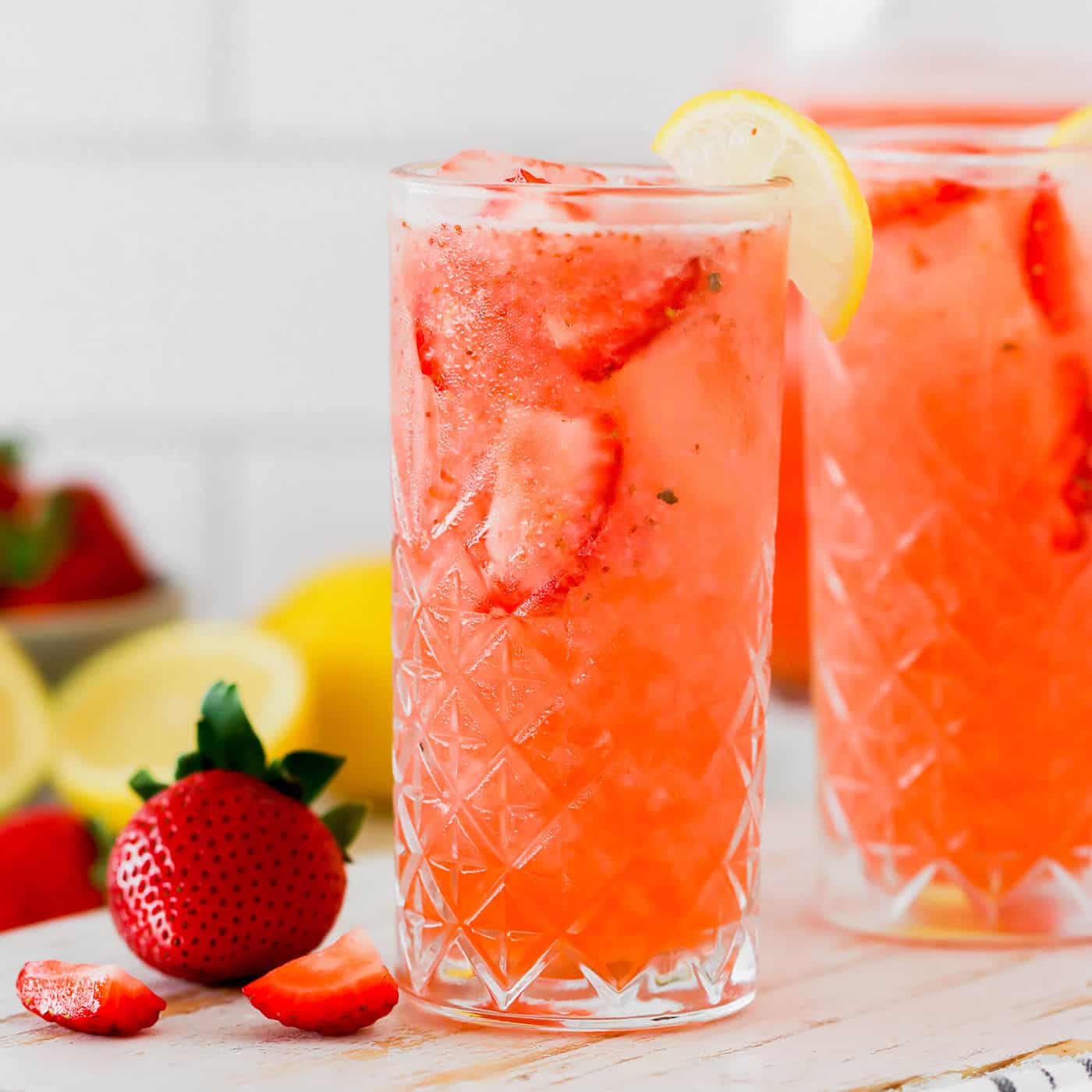 glasses of strawberry lemonade, plus fresh lemons and strawberries
