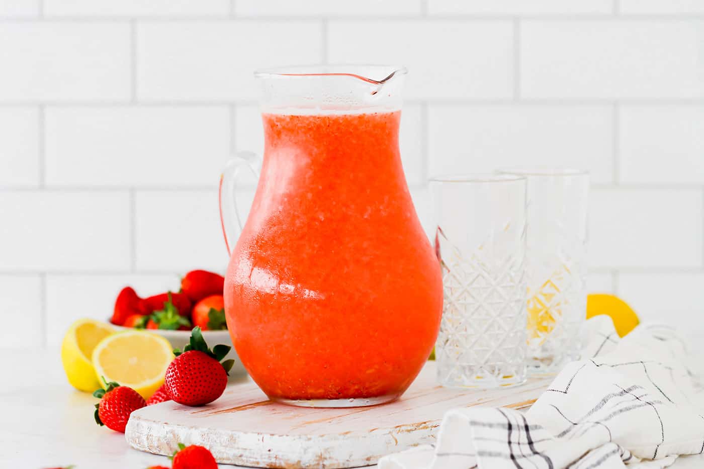 glass pitcher of strawberry lemonade, plus fresh lemons and strawberries