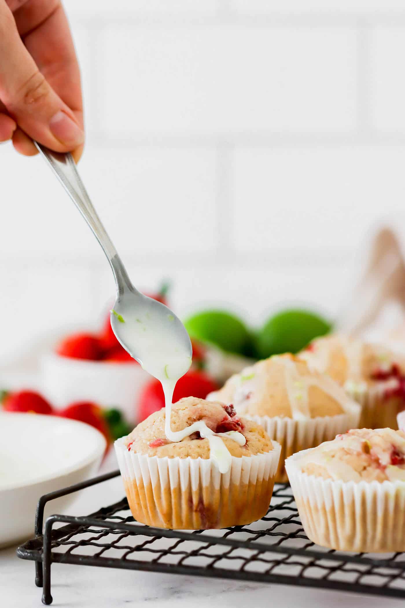 fresh strawberry muffins on a wire cooling rack, with a spoonful of lime glaze being added over the top