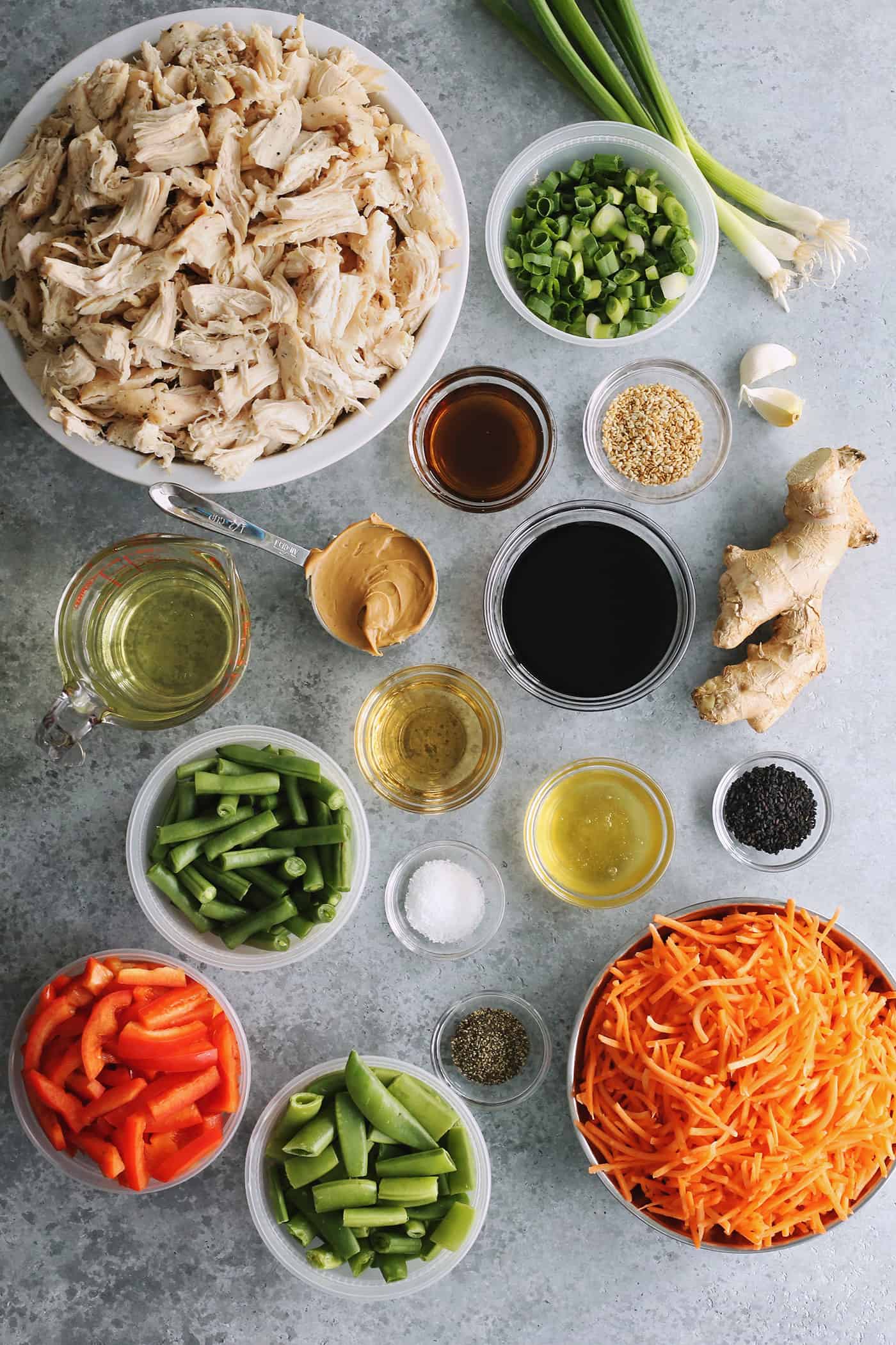 ingredients to make Chinese chicken salad, to include shredded chicken, fresh pea pods, red pepper, carrot, and green beans, plus a creamy peanut dressing