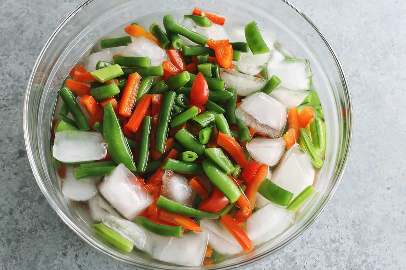 green beans, pea pods, and red pepper in a clear bowl (ice bath)