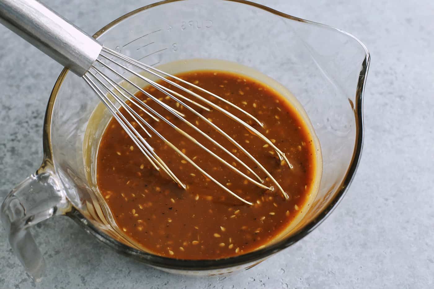 a large glass measure filled with a creamy peanut sauce, plus a whisk