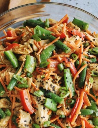 chicken salad with fresh veggies and a peanut butter dressing, in a clear serving bowl