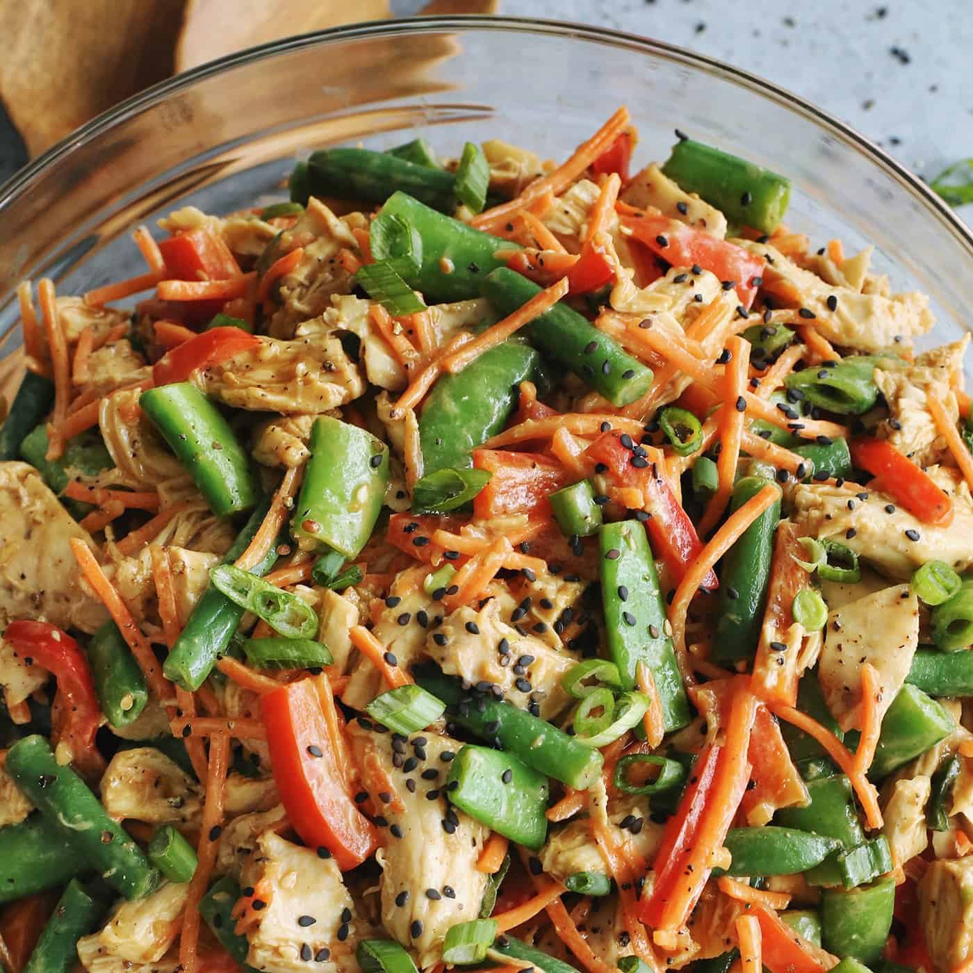 chicken salad with fresh veggies and a peanut butter dressing, in a clear serving bowl