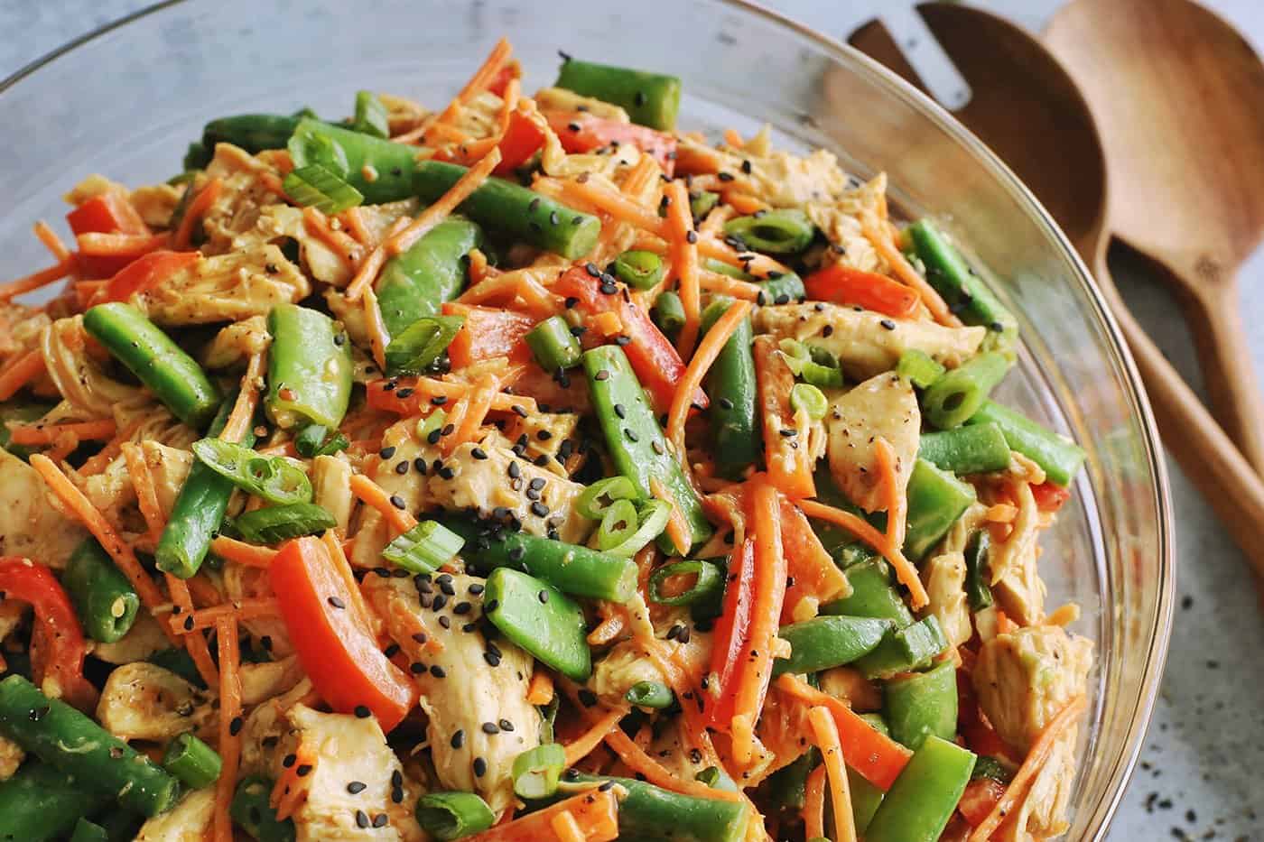 a large clear bowl of salad made of shredded chicken and chopped vegetables tossed with a peanut dressing