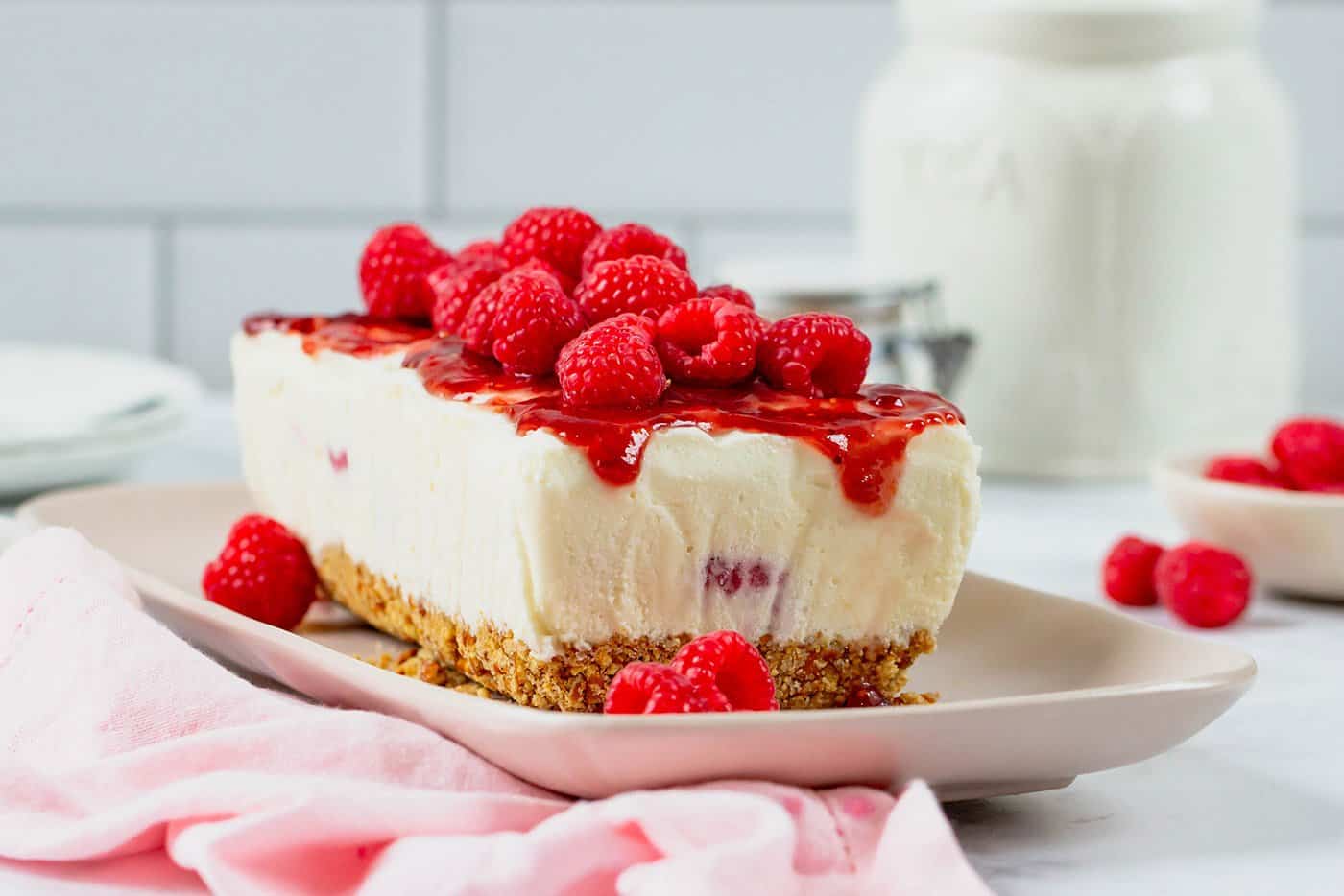 a platter holding a frozen dessert with a pretzel crust, creamy center with fresh raspberries, and raspberry sauce topping