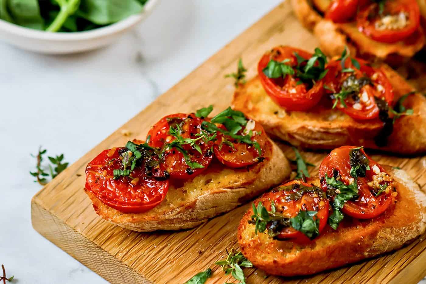 roasted tomatoes on slices of toasted baguette, on a wooden cutting board