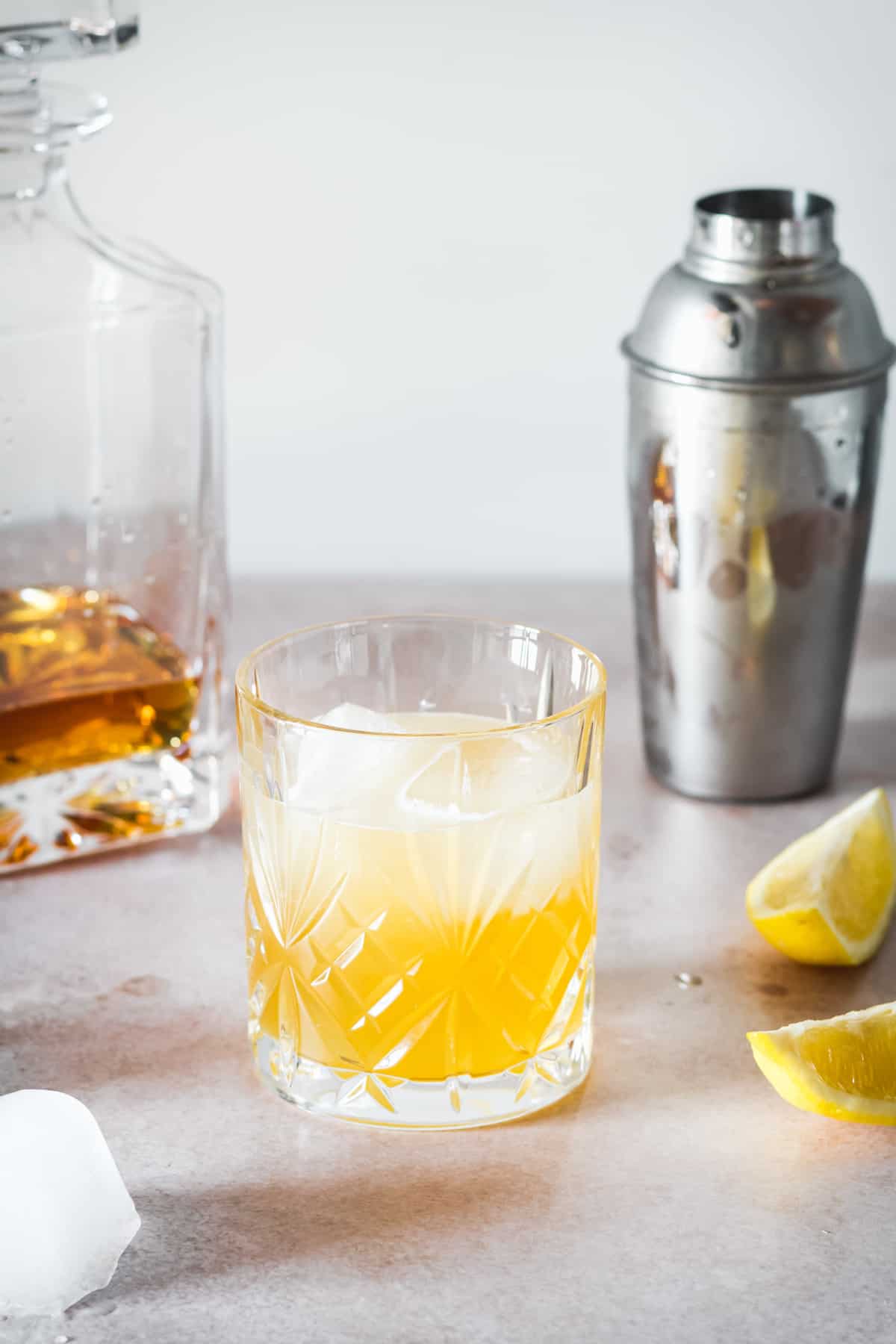 A whiskey sour over ice in front of a bottle of whiskey and a shaker