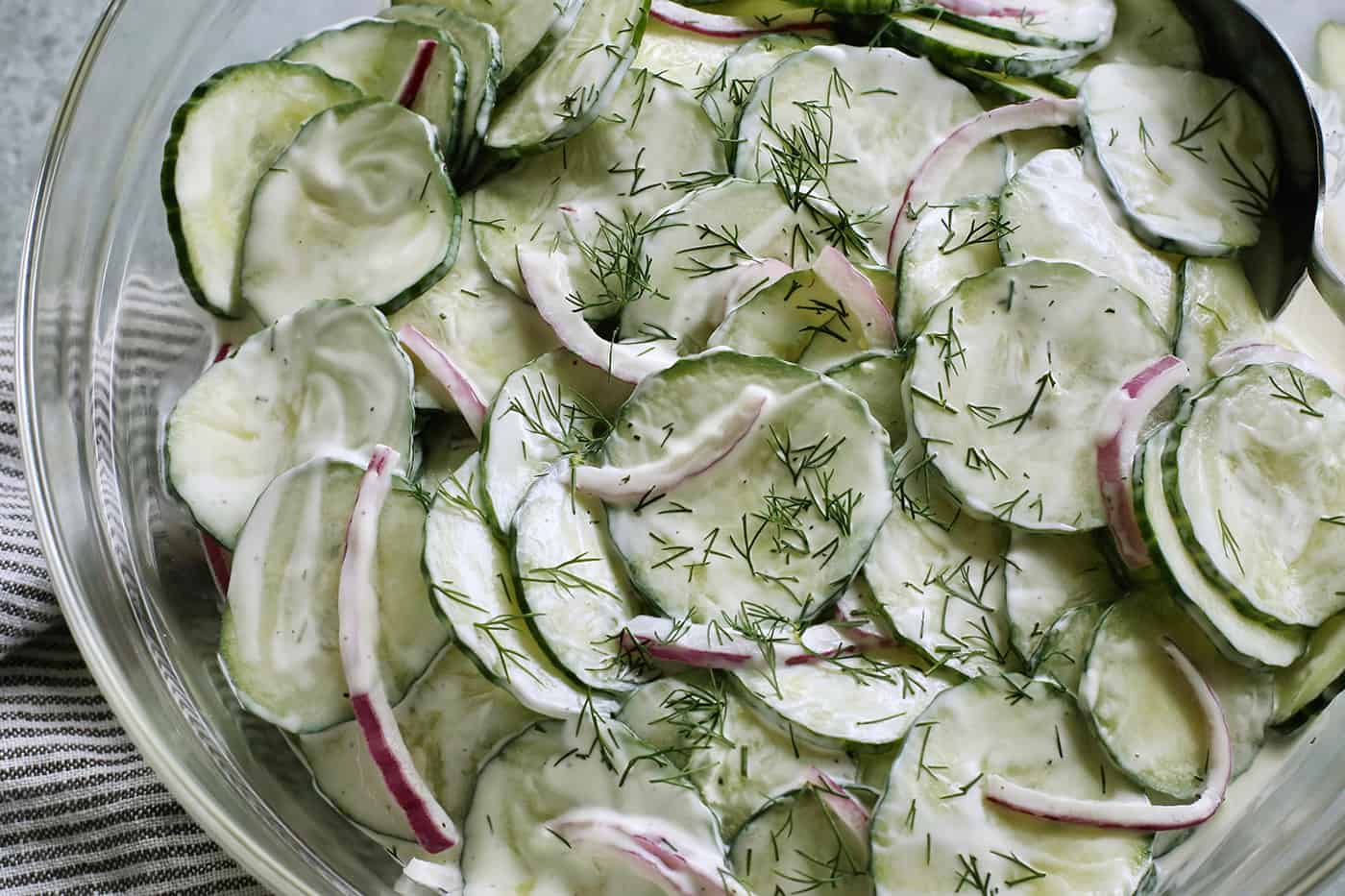 close-up photo of creamy cucumber salad in a clear serving bowl