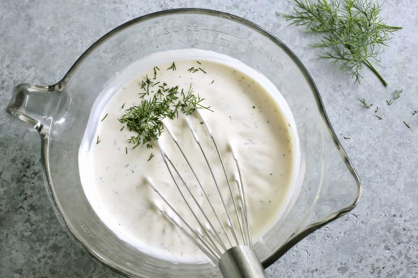 mixing creamy dressing in a clear spouted bowl, with a wire whisk