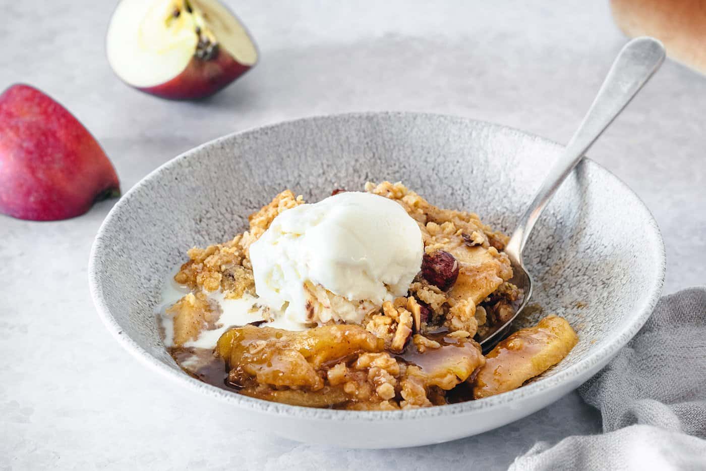 apple crisp with caramel and almond in a low wide gray bowl, plus a scoop of vanilla ice cream