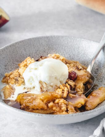 apple crisp with caramel and almonds in a low wide gray bowl, topped with a scoop of ice cream