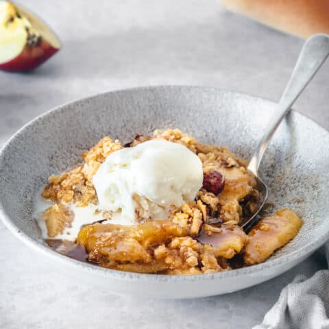 apple crisp with caramel and almonds in a low wide gray bowl, topped with a scoop of ice cream