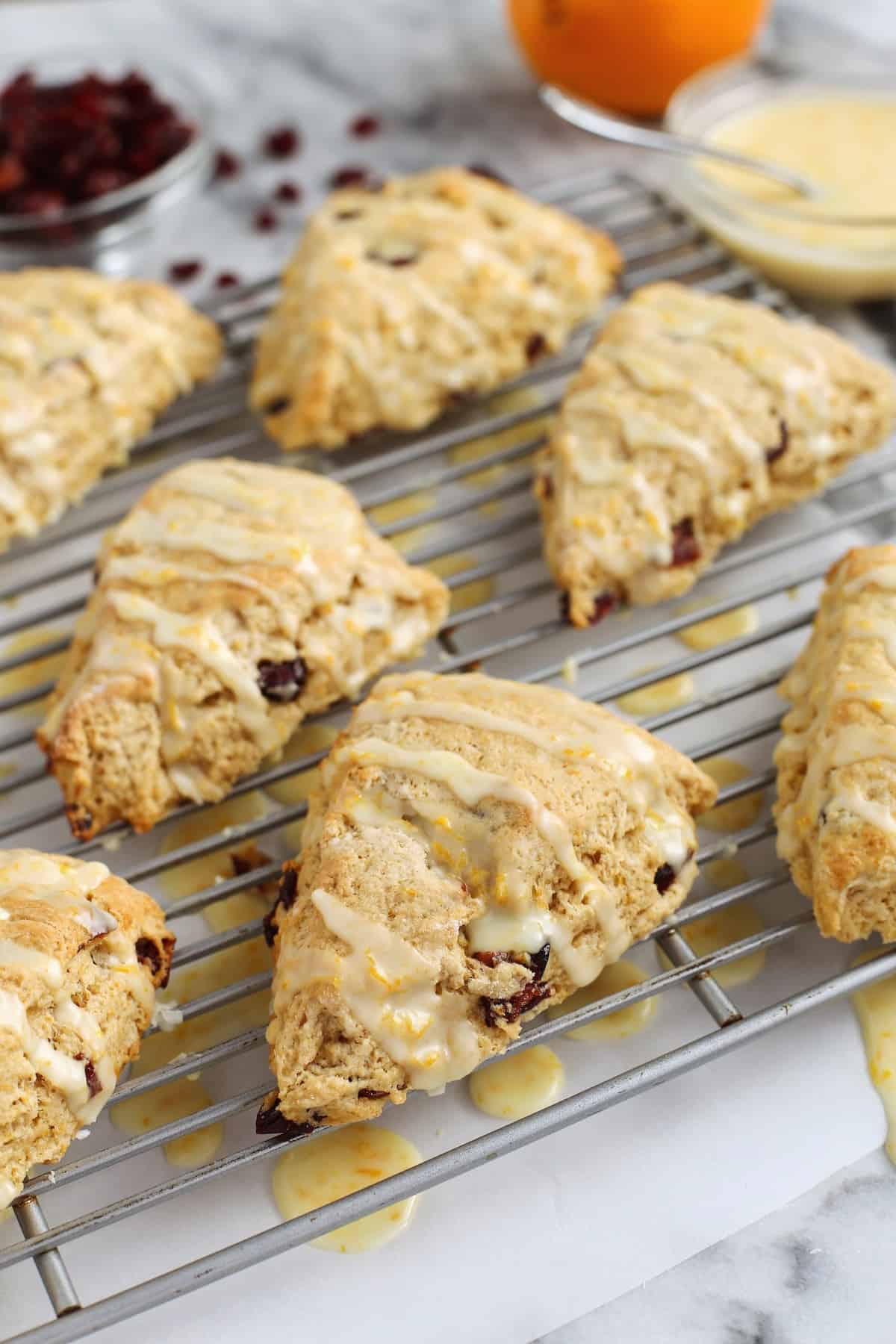 Glazed cranberry orange scones on a wire rack with a bowl of glaze in the background.
