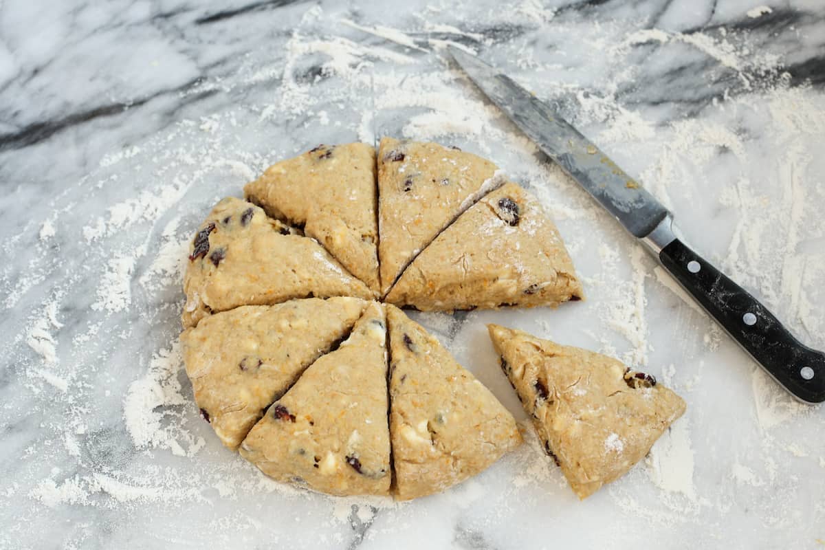 Scone dough cut into wedges on a marble countertop next to a large knife.