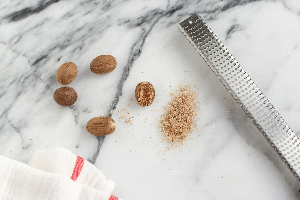 Whole nutmeg, ground nutmeg, and grater on marble slab