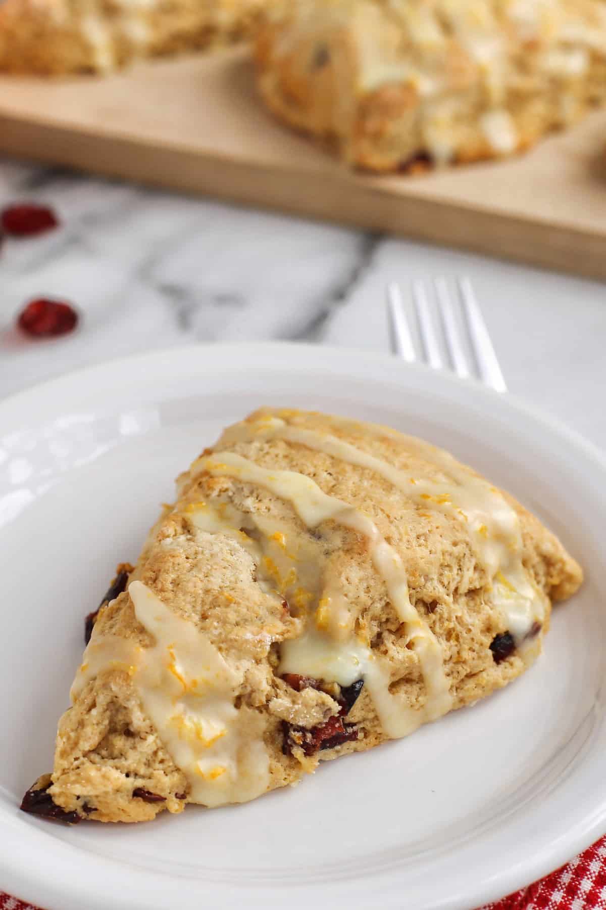 Cranberry Orange Scone with Orange Nutmeg Glaze on white plate with scones on cutting board in background